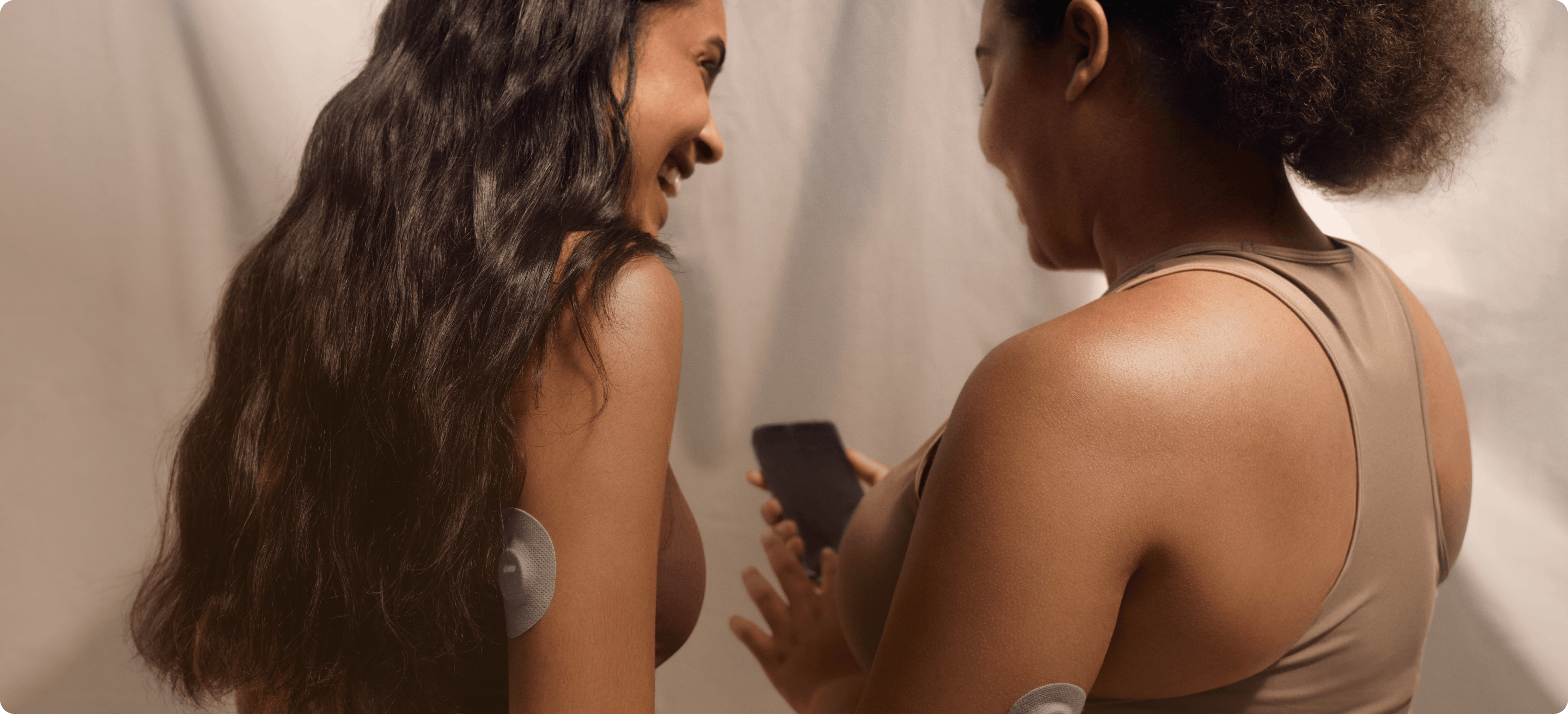 woman showing smiling friend her health improvement from monitoring blood sugar with Veri